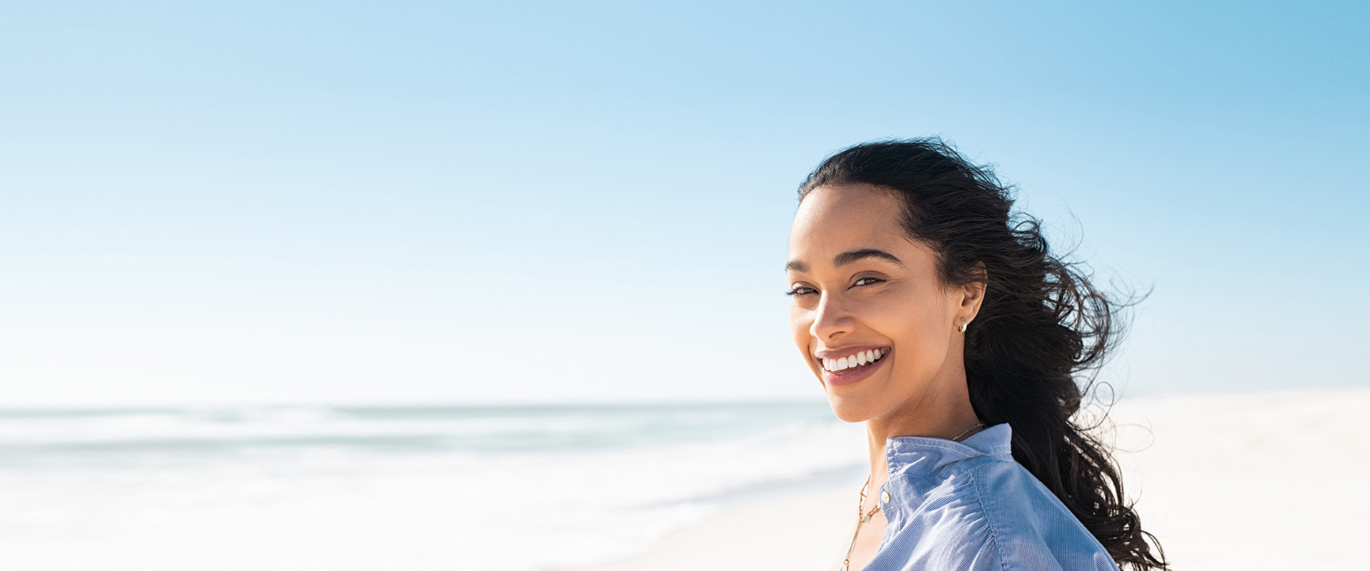 The image features a woman with a radiant smile, standing on a beach under a clear sky.