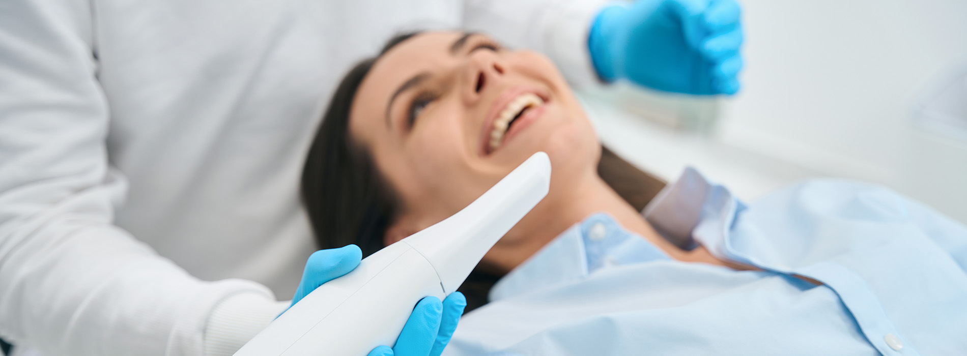 The image shows a person receiving dental care, with a dental professional performing work on their teeth while the patient is seated in a dental chair.