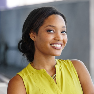 A woman with a radiant smile, wearing a yellow top and posing for the camera.