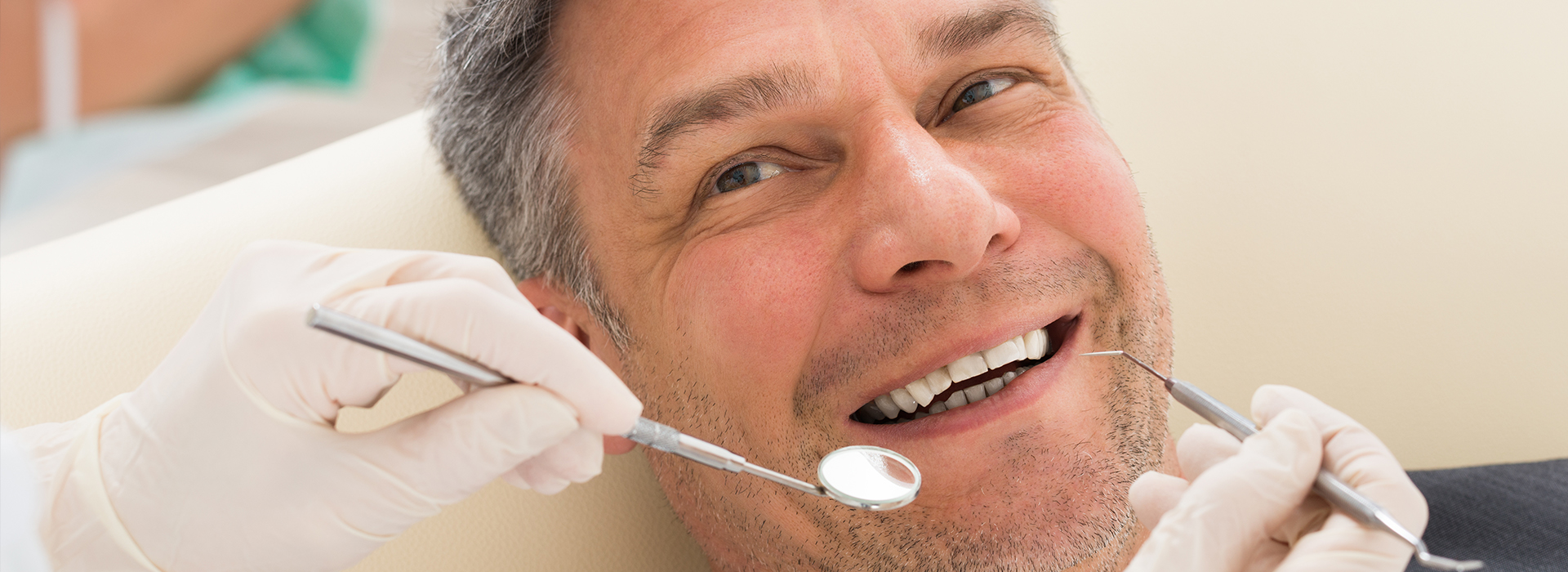 The image depicts a man sitting in a dental chair, receiving dental care with a smile on his face.