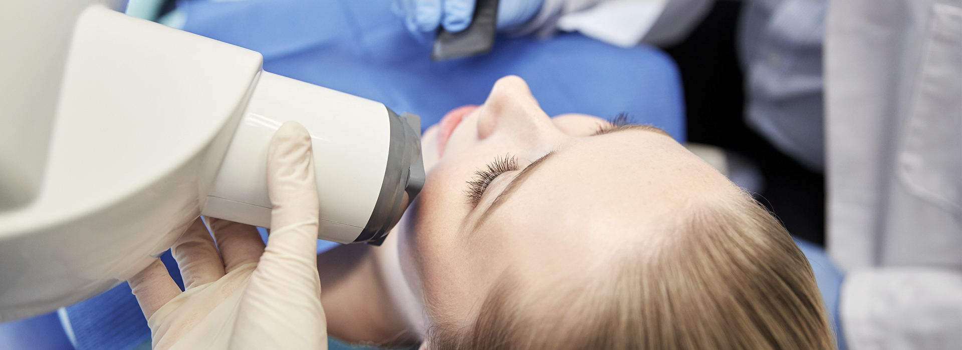 The image shows a person receiving dental care, with a dentist using a microscope to examine their teeth.