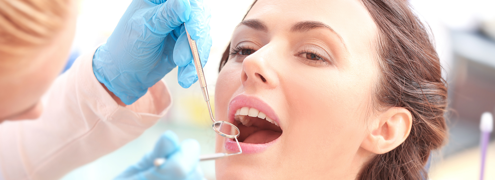 The image is a photograph featuring a woman receiving dental treatment, with a dental professional performing the procedure using instruments and a syringe.