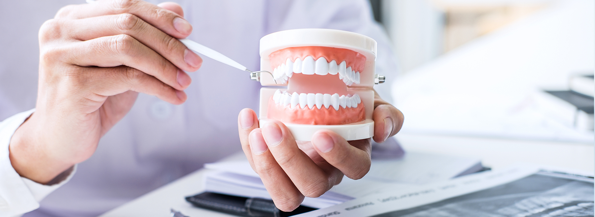 This is a photograph of a person s hand holding a cup with a toothbrush inside, placed on a desk in front of a computer screen.