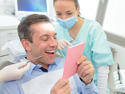 Man holding a pink card in front of his face, surrounded by dental equipment and two smiling individuals.