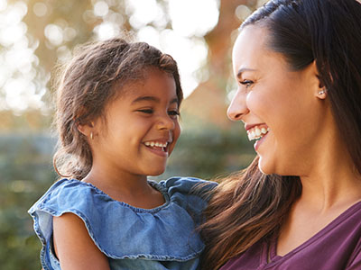 A woman and a child, both smiling, sharing an outdoor moment.