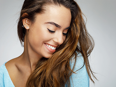 The image is a close-up portrait of a woman with long, wavy hair smiling at the camera.