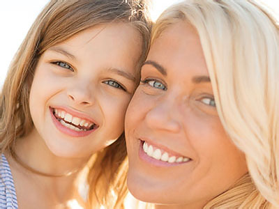 A woman and a child smiling at the camera, with the woman s face partially obscured by her hair.