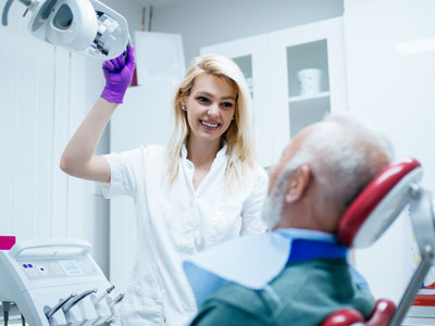 Dental hygienist assisting elderly patient in dental chair.