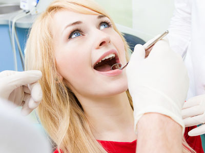 The image shows a woman in a dental chair receiving dental care, with a dental professional using a drill on her teeth and the patient holding her mouth open.