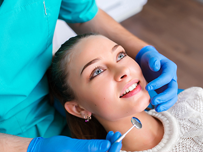 The image depicts a dental professional performing a procedure on a patient, with the patient smiling and looking at the camera.