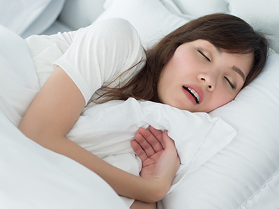 A woman sleeping in bed with a pillow over her mouth, suggesting she is asleep or possibly experiencing discomfort.