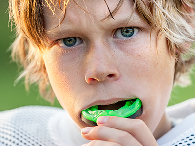 Blonde boy with green mouthguard, looking directly at the camera.